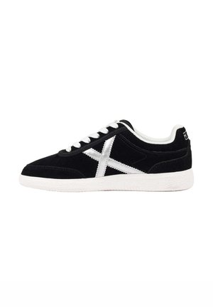 Zapatilla negra de corte bajo con cordones blancos, suela blanca y un diseño en forma de X blanco en el lateral.