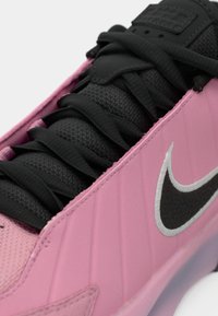 Nike sneaker ar gludu rozā sintētiskā augšdaļu ar ribotu tekstūru, melnu tīkliņa mēli un melnām auklām. Sudraba Swoosh logotipa detaļa.
