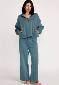 Turquoise fleece pullover met een ritssluiting tot een kwart en twee frontzakken, gecombineerd met bijpassende wijde broek met een elastische tailleband.