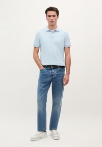 Lyseblå polo-shirt med korte ærmer, parret med lige ben lyseblå jeans. Hvide sneakers og et sort bælte fuldender outfittet.
