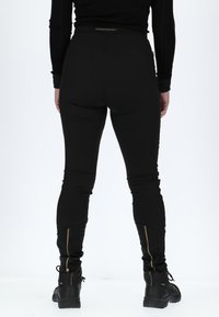 Schwarze, sportliche Hosen mit hohem Bund, schmaler Passform, Reißverschluss-Details an den Knöcheln und einem Logo auf dem hinteren Bund. Dehnbarer, glatter Stoff.