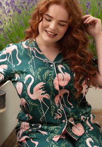 Piżama w zielonym kolorze z wzorem flamingów, z różowymi flamingami i liściastymi akcentami. Wykonana z miękkiego materiału, z zapięciem na guziki.