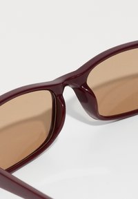 Solsikkerglas med en dyp burgunder plastinnfatning og brune tonede linser, med en moderne, kantet design og jevn finish.