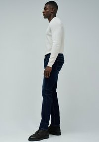 Jeans de color azul oscuro con un corte ajustado y cinco bolsillos, combinados con una blusa blanca de manga larga con relieve. El calzado son botas oscuras con cordones.