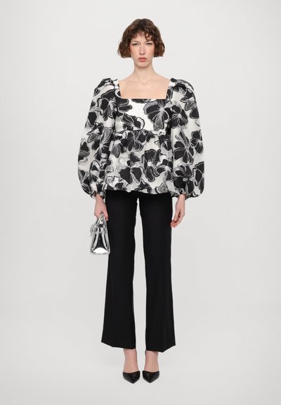 Blusa de algodón blanca y negra con estampado floral, mangas abullonadas, escote cuadrado, combinada con pantalones negros rectos y un pequeño bolso de mano plateado.