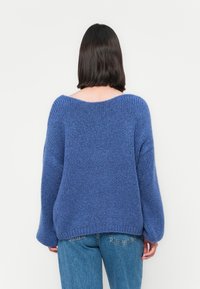 Maglione oversize in materiale a maglia di un blu chiaro, con scollo ampio, spalle scese e polsini a costine, abbinato a jeans a vita alta.