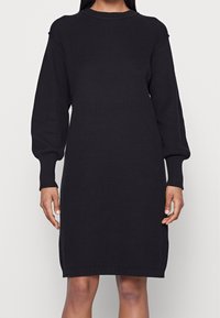 Abito nero a maglia a coste con maniche lunghe, scollatura a girocollo e una vestibilità morbida. Presenta un tessuto strutturato e una silhouette dritta.