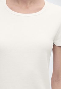 Κοντινό πλάνο ενός ατόμου που φοράει ένα απλό λευκό κοντομάνικο μπλουζάκι με στρογγυλή λαιμόκοψη.