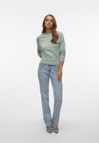 Pull en tricot vert menthe avec un col rond et un ourlet côtelé, associé à un jean droit bleu clair et des escarpins bleu clair à bout pointu.