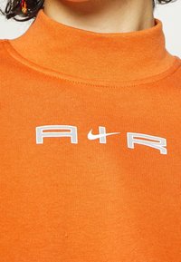 Orange högkragad sweatshirt i bomullsblandning med texturerad finish, med en vit logotyp "A4R" och Nike swoosh som accentuerar bröstområdet.