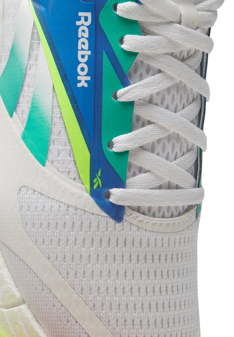 Zapatilla deportiva blanca con material de malla, acentos multicolores en azul y verde, y cordones planos blancos. Logotipo de Reebok visible.