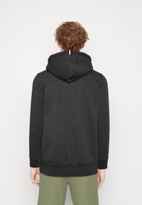 Grijze hoodie met een losse pasvorm, gestructureerde stof en een driekleurige accentdetail op de achterkant van de capuchon.