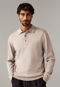 Beige långärmad polo skjorta med krage, treknapps knäppning, ribbade ärmslut och fåll. Mjuk textur med subtil färgvariation.