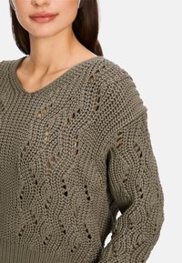 Strickpullover in Olivgrün mit einem lockeren, strukturierten Muster und einem weiten V-Ausschnitt. Verfügt über offene Maschen und gerippte Bündchen für einen entspannten Sitz.