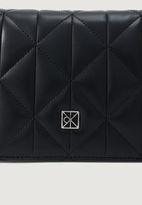 Μαύρο πορτοφόλι από καπιτονέ δέρμα με γεωμετρικό σχέδιο, ασημένια μεταλλικά στοιχεία με λογότυπο και αντίθεση στη ραφή για υφή και λεπτομέρεια.