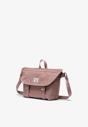 Borsa a tracolla in tessuto rosa con pattina, patch logo frontale, tracolla regolabile e due chiusure a fibbia frontali. Zip sulla parte superiore.