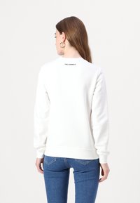 Felpa bianca con collo rotondo e maniche lunghe, caratterizzata da un piccolo logo nero "KARL LAGERFELD" sul retro. Tessuto morbido.