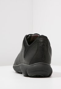 Black leather sneaker with mesh detailing, rounded heel, and textured outsole. Features logo on the side and minimalist design.