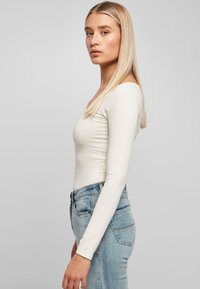 Bodysuit blanco de manga larga con escote redondeado, combinado con unos vaqueros ajustados de denim de color azul claro. Textura suave y diseño ajustado.