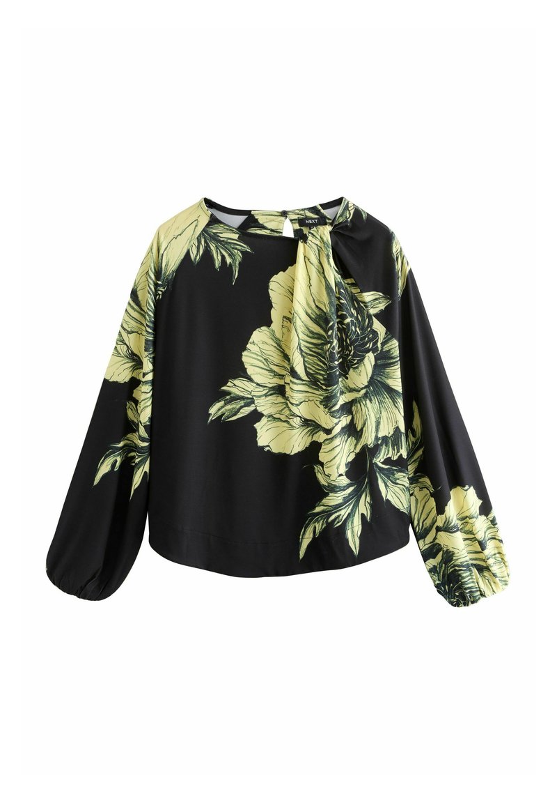 Melna blūze ar lieliem dzelteniem ziedu rakstiem, gariem balona tipa piedurknēm un mīkstu tekstūru. Raksturīga kakla daļa ar saistāmu mezglu, kas piešķir papildu dizaina elementu.