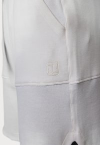 Weiße, strukturierte Shorts mit einem gerippten Muster, einem gestickten Logo in einer kontrastierenden Farbe an der Seite und einem kleinen Ausschnitt.