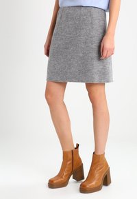 Jupe A-line en mélange de laine gris avec des plis sur le devant, associée à des bottines tan à talons block et fermetures éclair sur le côté.