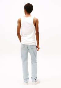 Hvit bomulls tanktop og lyseblå denimjeans, iført med hvite sneakers. Utsikt fra bak, som fremhever den avslappede passformen og designet.