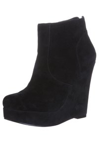 Botas de tobillo de ante negro con tacón en cuña, punta redondeada y textura suave. Presentan un diseño sin costuras y sin herrajes visibles.