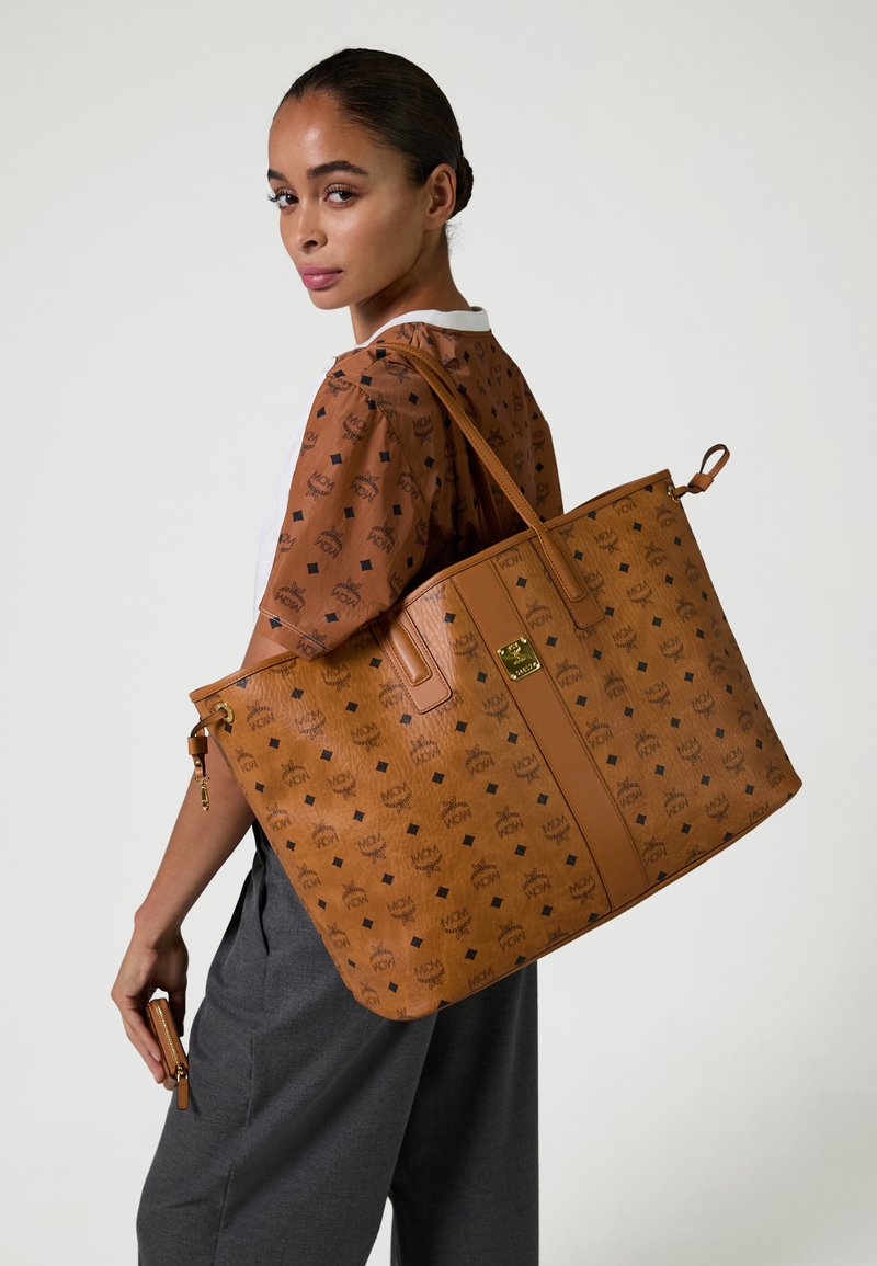 Grote beige totebag met een reliëfpatroon, met een gladde textuur, platte handvatten en een gouden hardware accent.