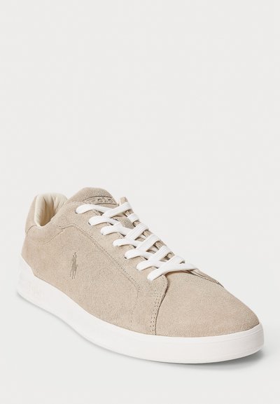 Baskets basses en daim beige avec des lacets blancs, un col rembourré et une semelle en caoutchouc blanche, arborant un logo brodé subtil sur le côté.
