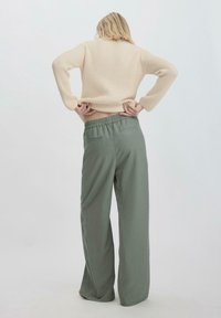 Beige geribbelde lange mouw trui gecombineerd met lichtgroene wijde broek; de broek heeft een elastische tailleband en achterzakken.