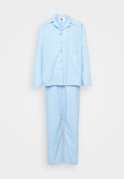 Svetlo modra pižama iz mehkega blaga; srajca z dolgimi rokavi z gumbom in žepom, v kompletu s širokimi hlačami z višinskim vzorcem.