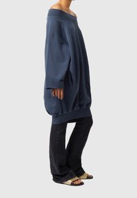 Överdimensionerad marinblå sweatshirt med off-shoulder halsringning och tumhålsknutar. Kombinerad med vida svarta jeans och beigea sandaler.