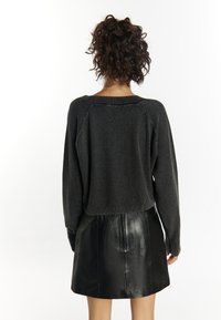 Schwarzer, kurzer Pullover mit strukturierter Strickoptik, weitem Rundhalsausschnitt und fallenden Schultern, kombiniert mit einem glänzenden schwarzen Leder-Minirock.