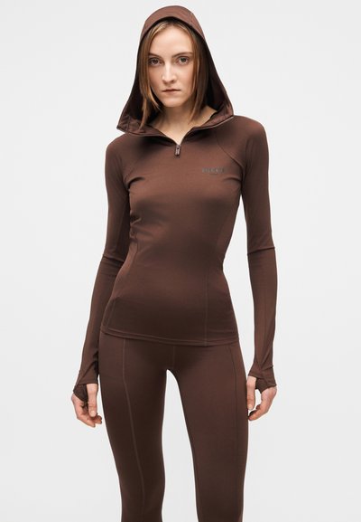 Rudas sportinis viršus su gobtuvu, turintis užtrauktuką prie kaklo ir skylutes nykščiams, derinamas su aptempiomis tamprėmis, visi pagaminti iš lygaus, tampraus audinio.