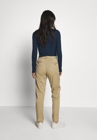 Chinos khaki con una vestibilità affusolata, dotati di tasche posteriori e una texture liscia. Abbinati a un top aderente a maniche lunghe blu navy e sneakers bianche.