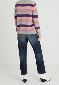 Szary sweter o fakturze z różowymi i fioletowymi poziomymi paskami, zestawiony z luźnymi ciemnoniebieskimi dżinsami i białymi botkami na obcasie.