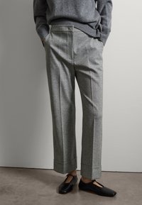 Pantalones de lana grises con un corte recto, que presentan pliegues frontales, bolsillos laterales y dobladillos vueltas, combinados con zapatos planos negros.