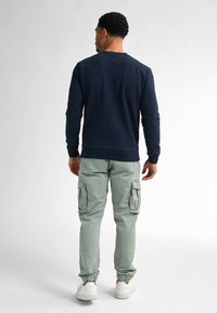 Marineblauw longsleeve shirt met ronde hals, gecombineerd met mintgroene cargobroeken met zijzakken en elastische boorden, en witte Sneakers.