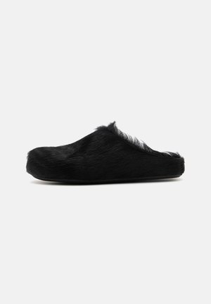 Pantofole foderate in pelliccia nera con punta arrotondata e retro basso. Presentano una tomaia morbida e strutturata e una suola piatta. Nessun hardware visibile.