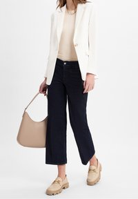 Bežový přiléhavý top, bílý blazer, tmavé džíny s cropped střihem a bežové slip-on boty s robustními podrážkami; nese světle bežovou kabelku.