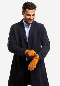 Leather gloves in tan, featuring a fitted design and stitching details. Worn by a person in a navy coat, showcasing a textured finish.