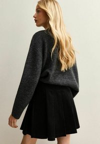 Morbido maglione grigio extra-large abbinato a una gonna nera plissettata in corduroy. Linee leggermente strutturate e fluide che vanno dalla parte superiore all'orlo svasato.