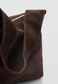 Braune Wildleder-Tote mit glatter Oberfläche, breite, weiche Griffe und einem silbernen Reißverschlussdetail oben.