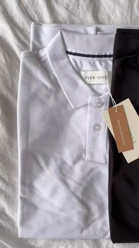 Bijela polo majica od teksturirane pamučne tkanine s tri dugmeta, složena iznad tamnih hlača s oznakom "reciklirani pamuk."