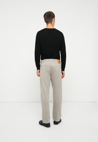 Light gray wide-leg pants made of cotton, featuring a textured black sweater. Noticeable stitched details and a tan leather patch on the back.