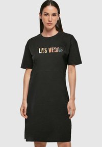 Svart bomull t-skjortekjole med korte ermer, med et grafisk "LAS VEGAS" i forskjellige farger over brystet og en enkel rett fasong.