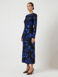 Svart långärmad klänning med blå blommönsterbroderi, figursydd midja och utsvängd kjol, stylad med spetsiga bruna klackar.