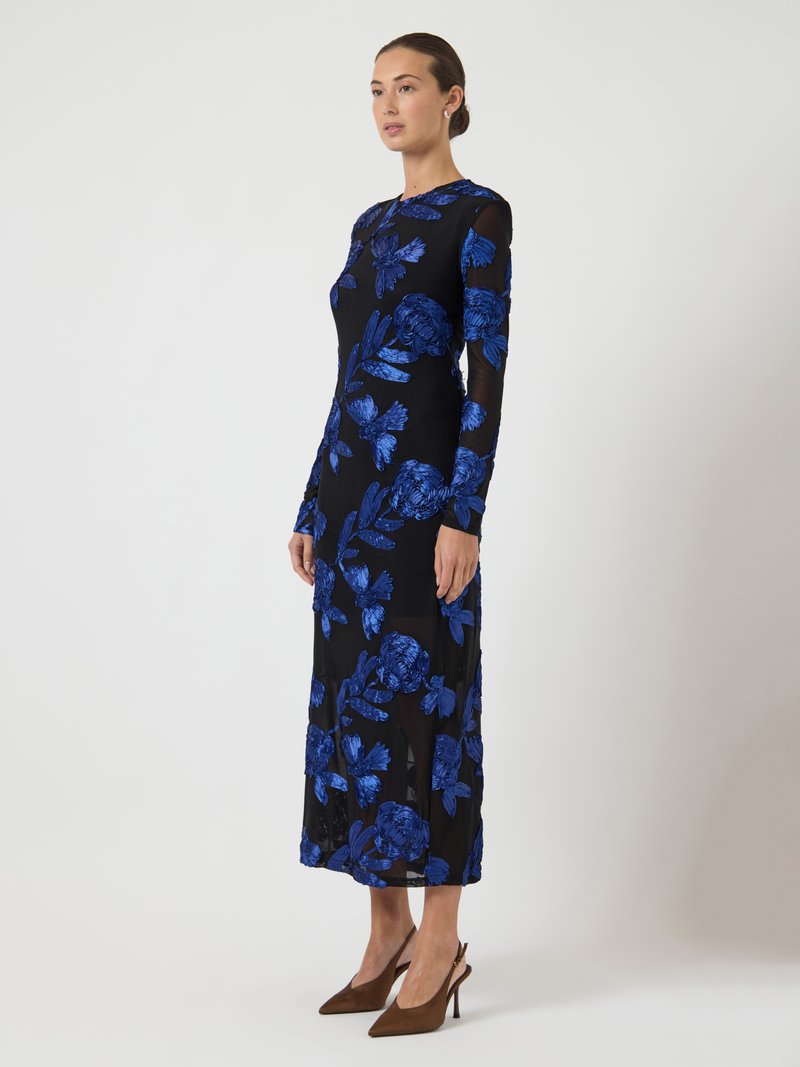 Svart långärmad klänning med blå blommönsterbroderi, figursydd midja och utsvängd kjol, stylad med spetsiga bruna klackar.