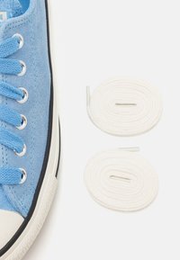 Modré semišové tenisky s bílou gumovou podrážkou a špičkou; obsahují modré tkaničky a vedle nich jsou dvě bílé tkaničky.